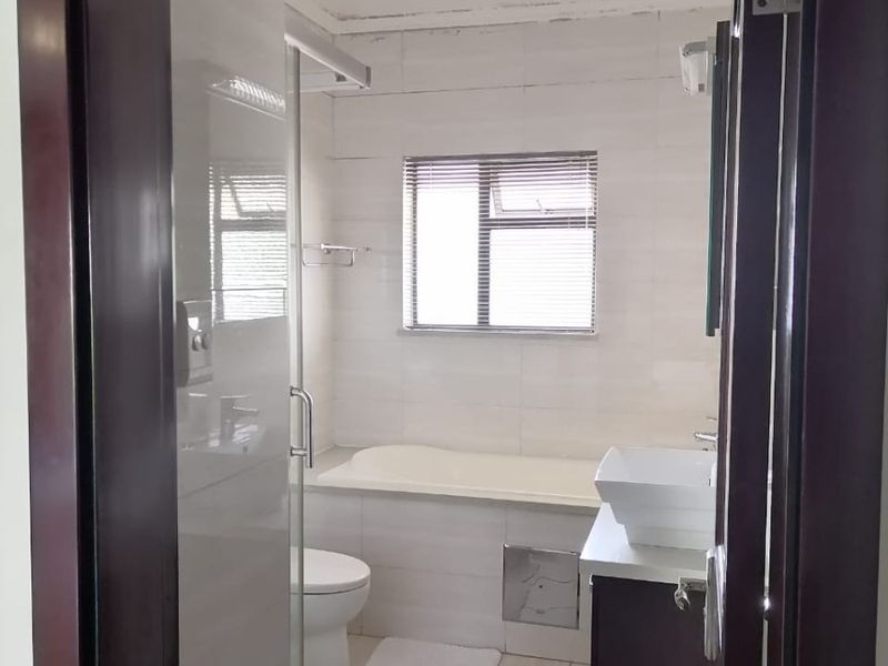 A functional bathroom featuring a built-in bathtub, glass shower enclosure, and a modern vessel sink vanity with tiled finishes.