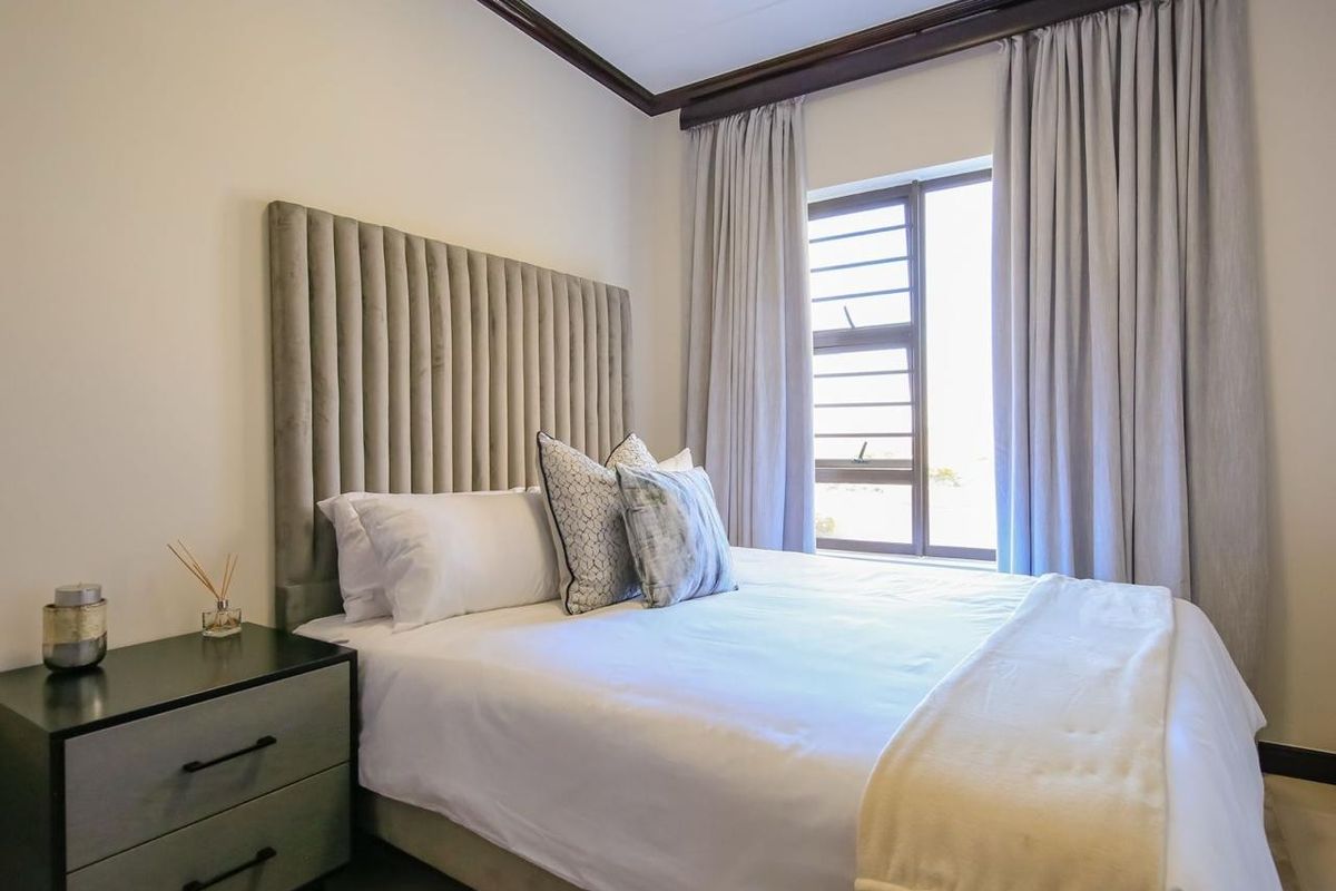 A well-maintained bedroom featuring neutral walls, dark coving, and an aluminium window frame with integrated curtain tracks.