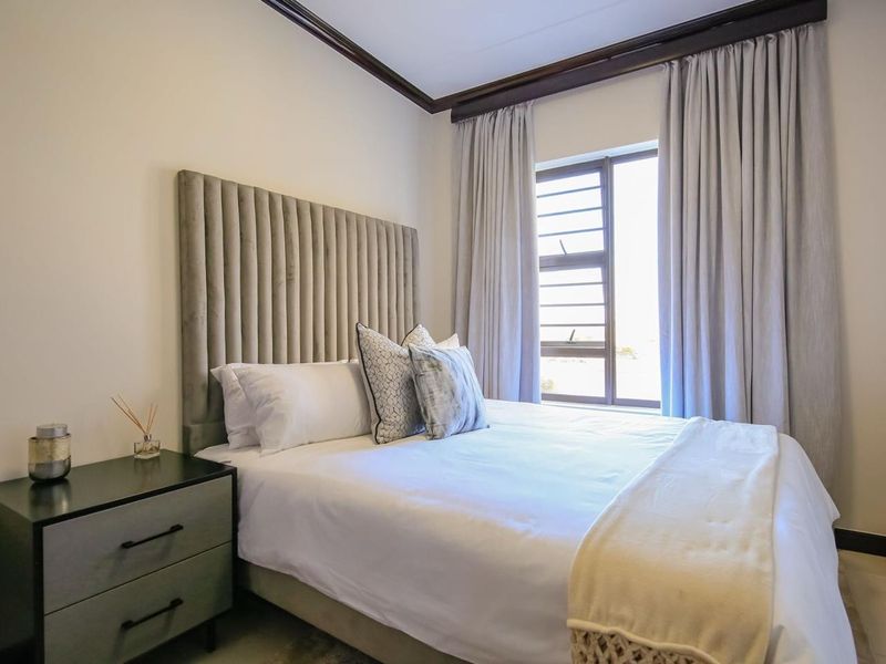 A well-maintained bedroom featuring neutral walls, dark coving, and an aluminium window frame with integrated curtain tracks.
