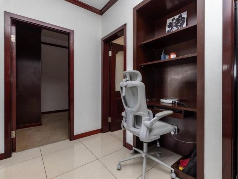 A functional home office nook featuring built-in timber desk and shelving, complemented by tiled flooring and dark wood door frames.