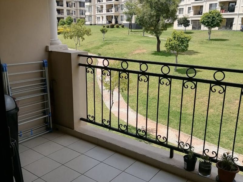 A covered balcony featuring tiled flooring and a decorative wrought iron balustrade, overlooking a well-maintained communal garden area.