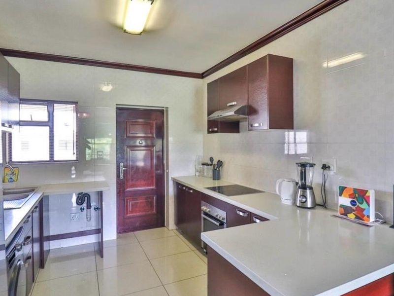 A functional kitchen featuring dark wood cabinetry, stone countertops, built-in oven and hob, extractor fan, and tiled finishes throughout.