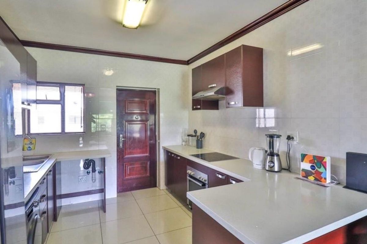 A functional kitchen featuring dark wood cabinetry, stone countertops, built-in oven and hob, extractor fan, and tiled finishes throughout.