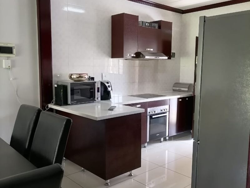 Open-plan kitchen featuring dark wood cabinetry, a built-in oven, hob, extractor fan, and light-colored tiled flooring, seamlessly connecting to the dining area.