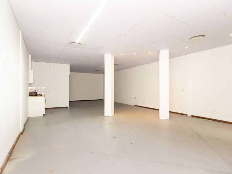 An open-plan retail space featuring a suspended ceiling, structural columns, and a small kitchenette area, suitable for various commercial business applications.