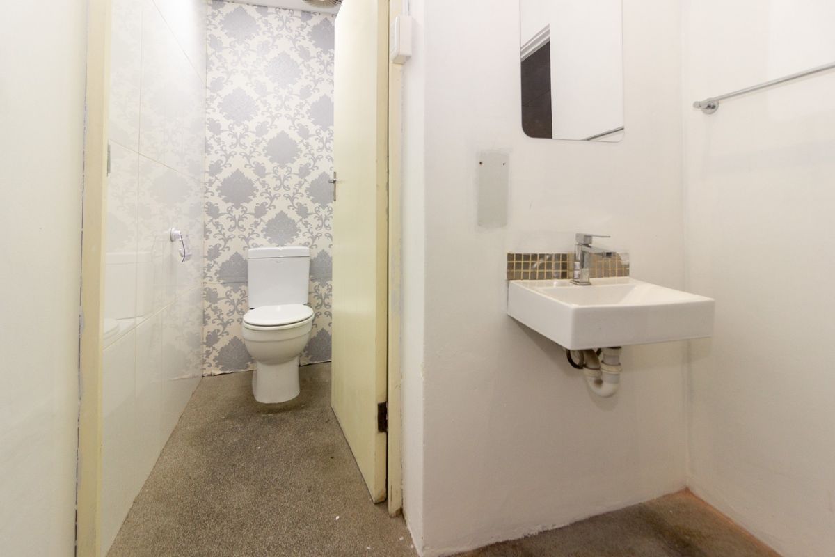 A compact bathroom featuring a wall-mounted basin, toilet, and simple finishes, currently in need of cosmetic updates and flooring repairs.