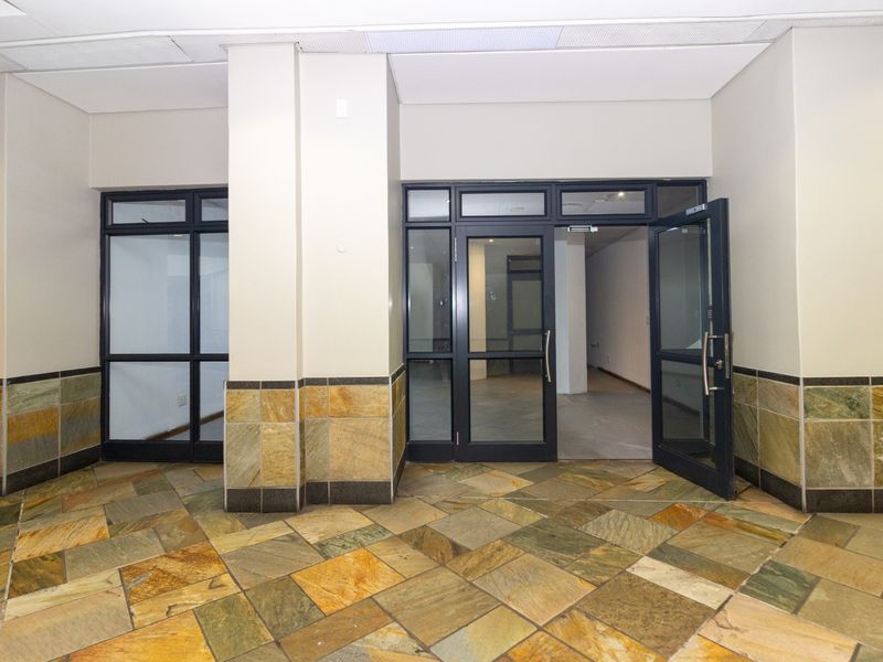 A clean, vacant commercial entrance area featuring stone tile flooring, stone wall accents, and glass-paneled doors leading into the main retail space.