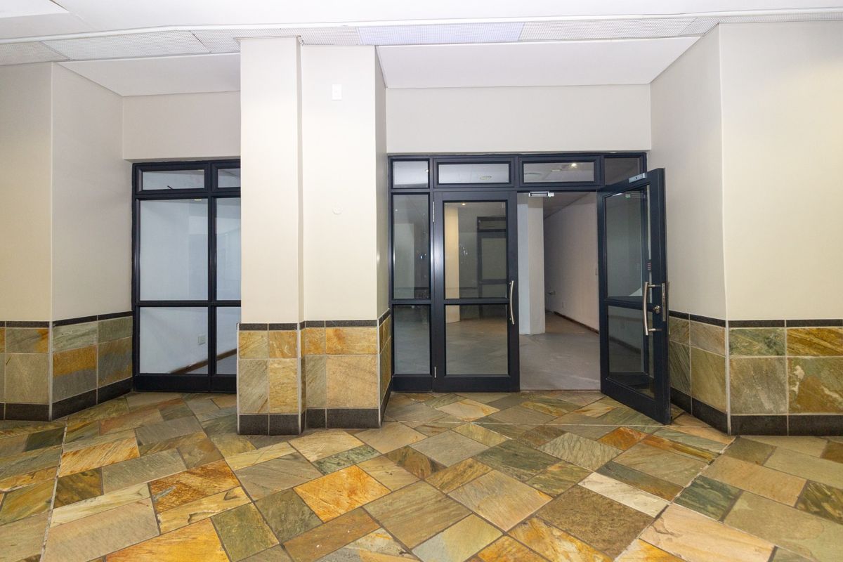 A clean, vacant commercial entrance area featuring stone tile flooring, stone wall accents, and glass-paneled doors leading into the main retail space.