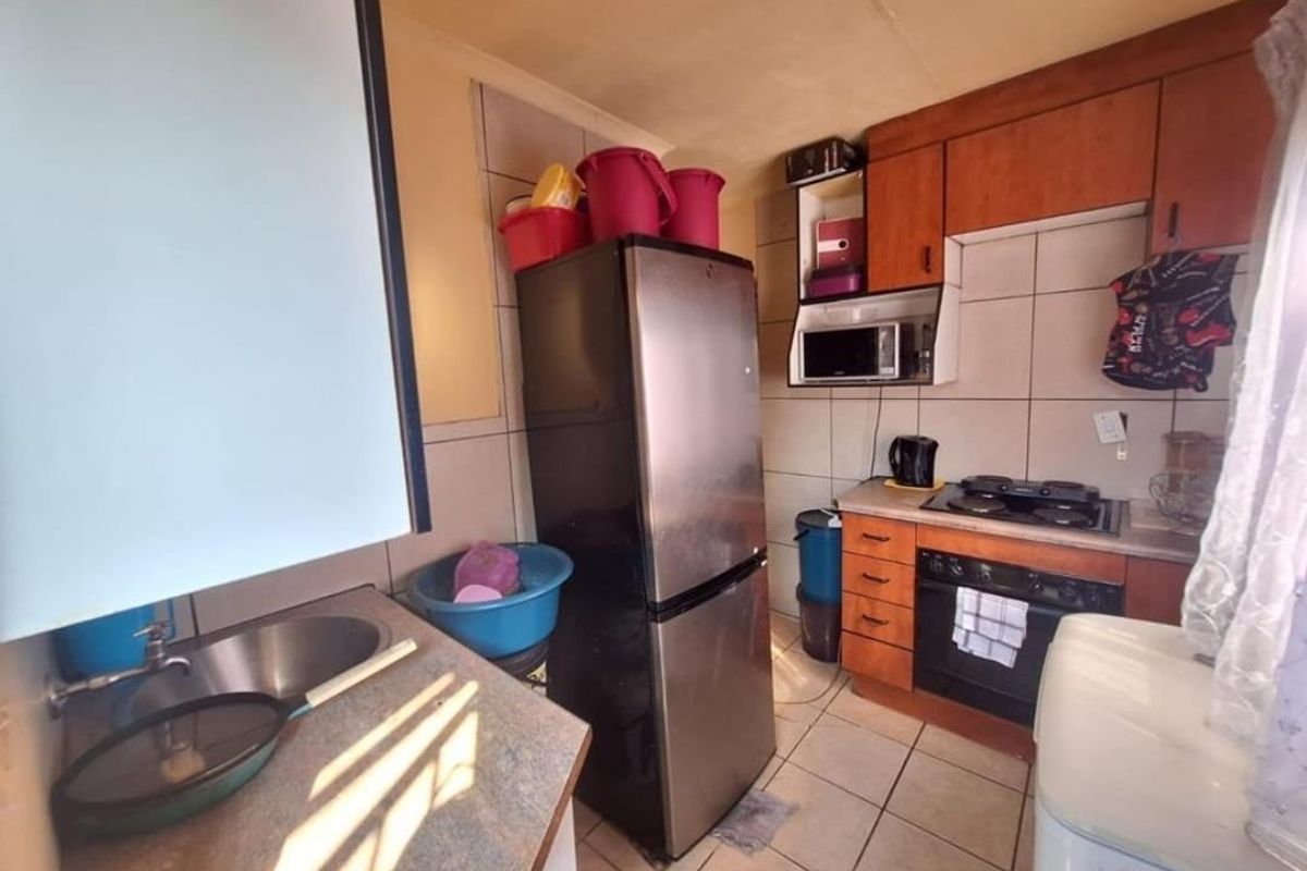 Compact kitchen featuring built-in wooden cabinetry, laminate countertops, a stainless steel sink, and integrated oven and hob with tiled splashbacks.