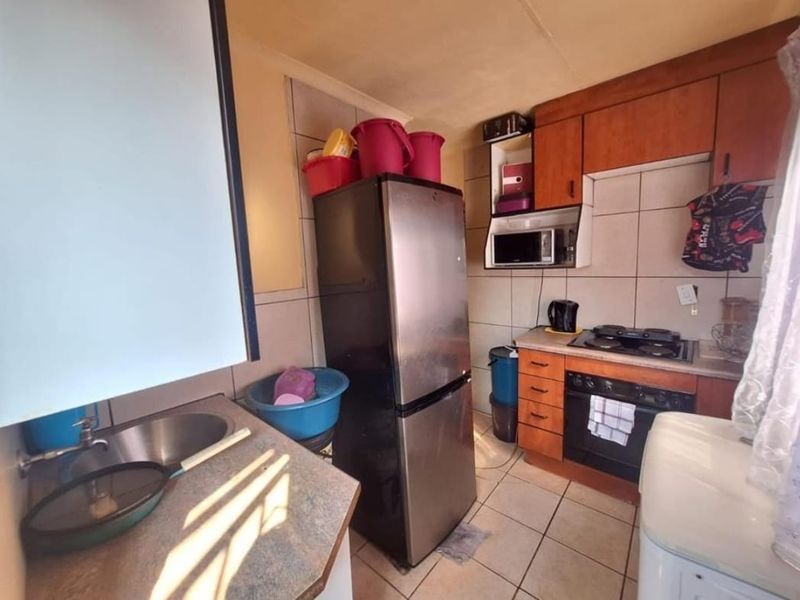 Compact kitchen featuring built-in wooden cabinetry, laminate countertops, a stainless steel sink, and integrated oven and hob with tiled splashbacks.