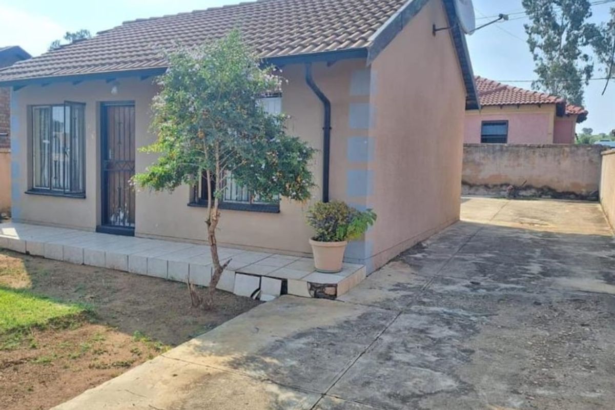 Front view of a single-story house featuring a tiled roof, security bars on windows, a security gate, and a concrete driveway.