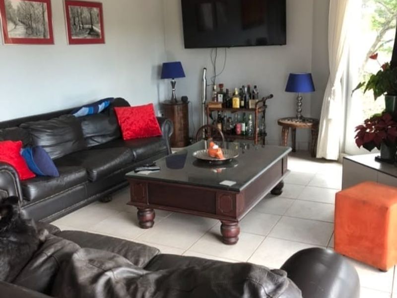 A comfortable living room featuring tiled flooring, a vaulted ceiling, and a sliding glass door providing natural light and garden access.