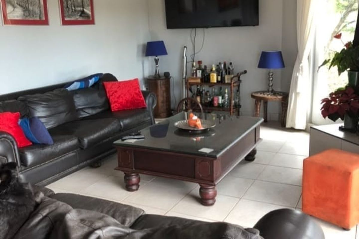 A comfortable living room featuring tiled flooring, a vaulted ceiling, and a sliding glass door providing natural light and garden access.