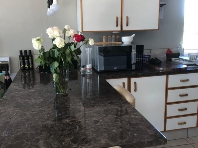A functional kitchen area featuring dark laminate countertops, white cabinetry with wood trim, and tiled flooring.