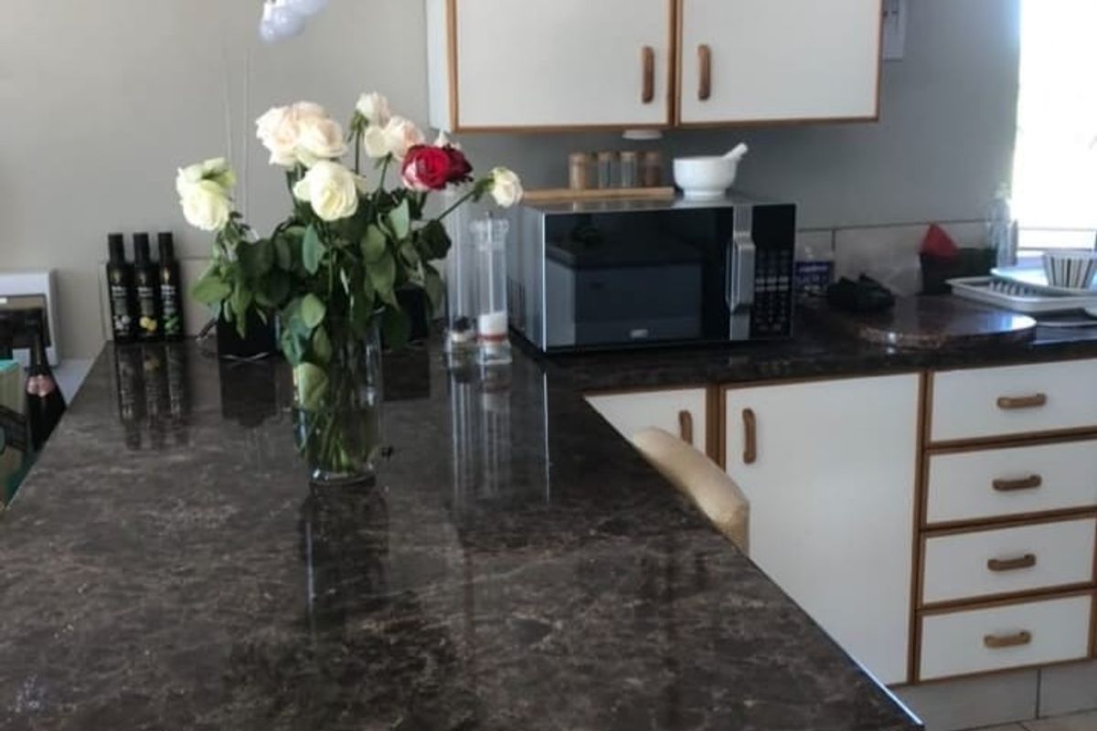 A functional kitchen area featuring dark laminate countertops, white cabinetry with wood trim, and tiled flooring.