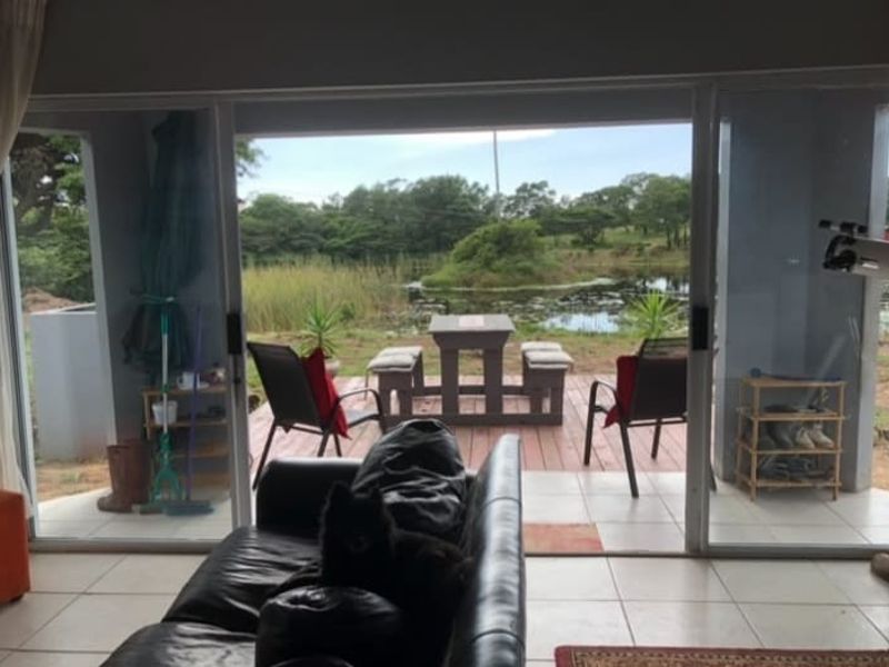 Living room featuring large sliding glass doors that provide seamless access to an outdoor patio area with scenic pond views.