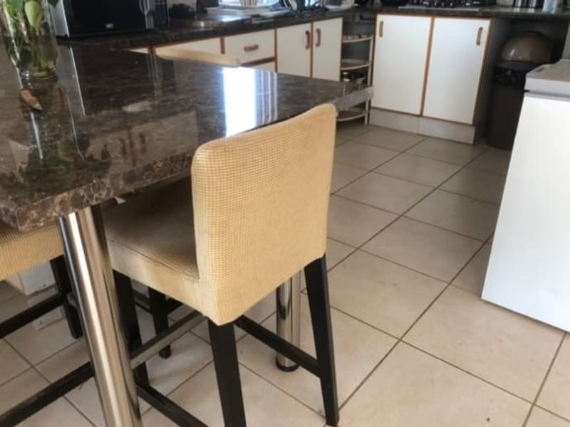A functional kitchen featuring a granite-topped breakfast bar, tiled flooring, and white laminate cabinetry with visible signs of wear.