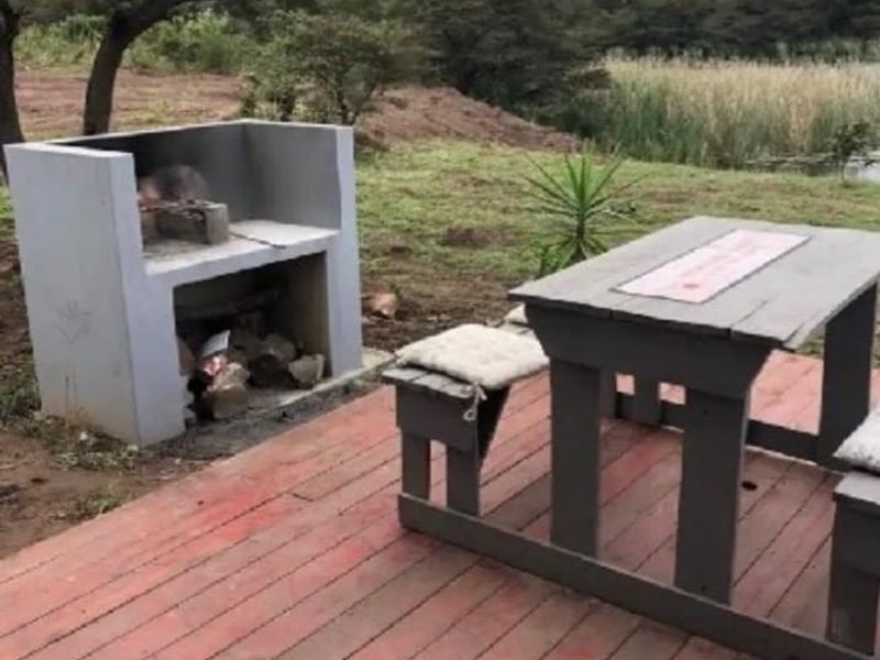 Outdoor patio area featuring a built-in masonry braai and timber decking, overlooking a natural landscape.