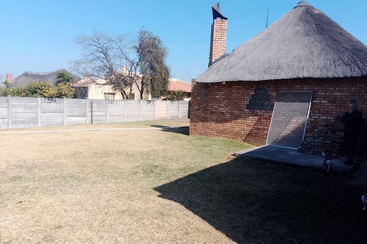 Rear garden view featuring a traditional thatch-roofed brick structure with a chimney and a precast concrete boundary wall.