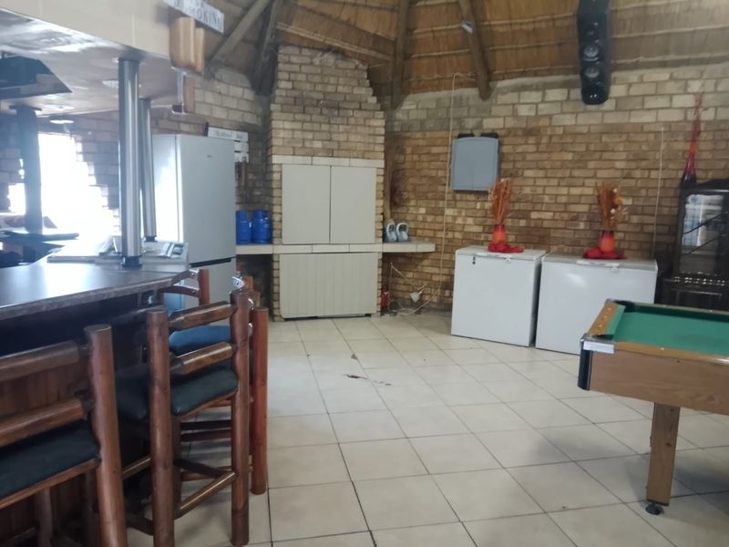 Rustic entertainment area featuring a built-in bar, brick fireplace, and traditional thatched roof, offering a cozy space for social gatherings.