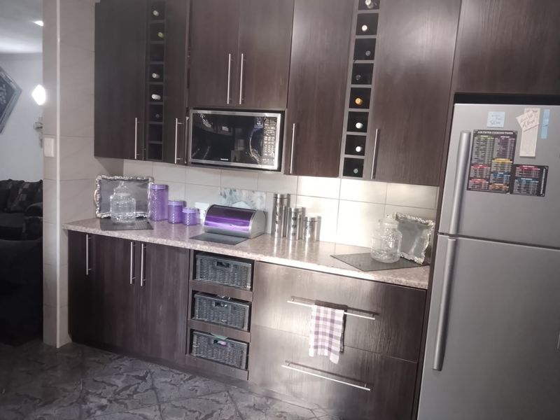 A functional kitchen featuring dark wood cabinetry, built-in microwave, laminate countertops, and tiled backsplash with integrated wine storage.