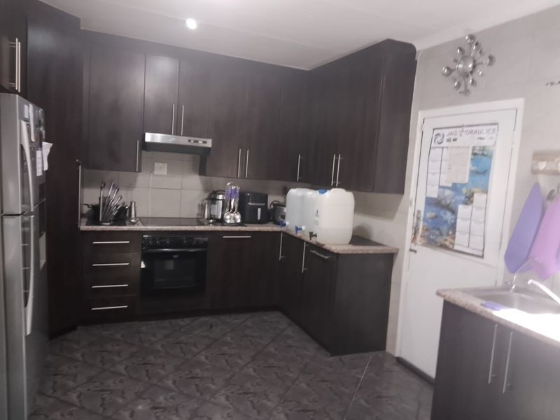 A functional kitchen featuring dark wood cabinetry, laminate countertops, built-in oven with extractor fan, and tiled flooring.