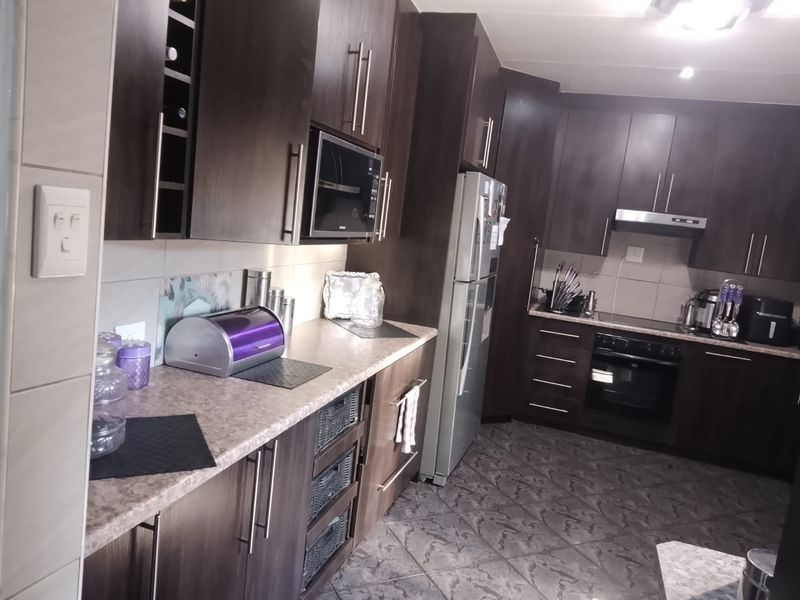 A functional kitchen featuring dark wood cabinetry, laminate countertops, built-in oven, hob, extractor fan, and tiled flooring.