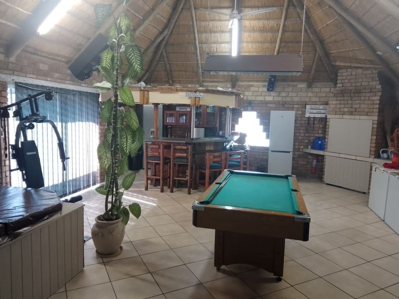 Spacious entertainment area featuring a thatched roof, exposed brick walls, tiled flooring, and a built-in bar counter, ideal for social gatherings.
