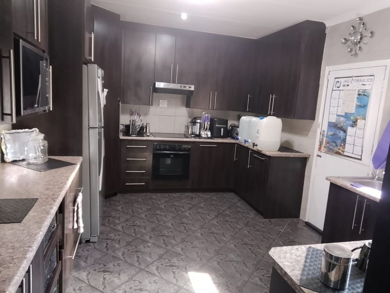 A functional kitchen featuring dark wood cabinetry, laminate countertops, and built-in appliances, including an oven, hob, and extractor fan.