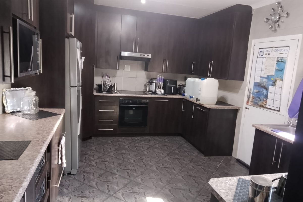 A functional kitchen featuring dark wood cabinetry, laminate countertops, and built-in appliances, including an oven, hob, and extractor fan.