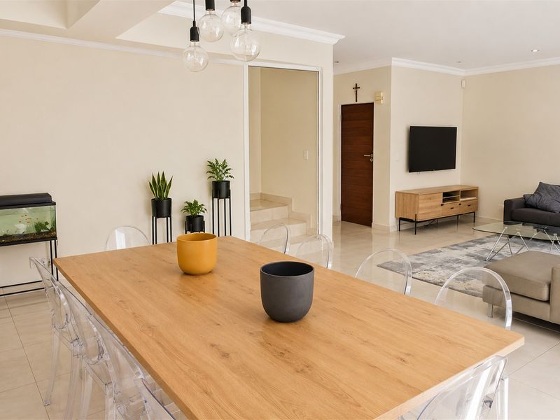 Spacious open-plan living and dining area featuring neutral walls, tiled flooring, and modern lighting fixtures, creating a bright and inviting atmosphere.