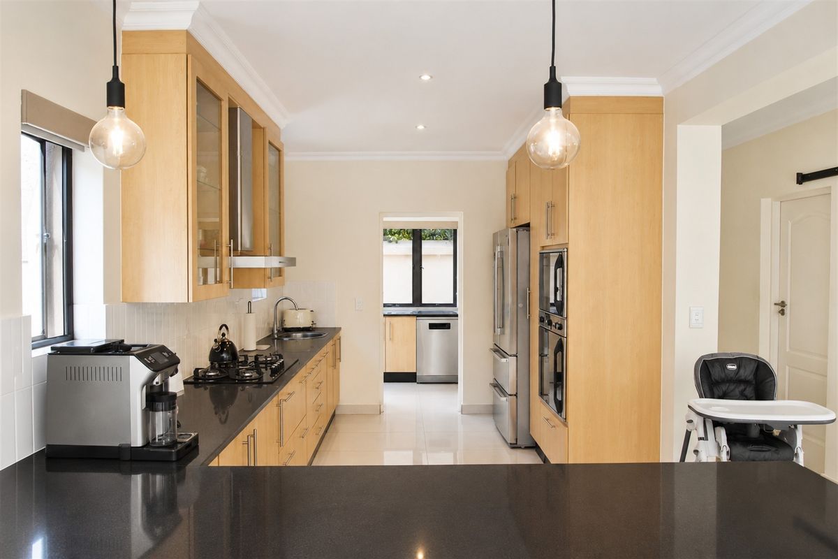 Modern kitchen featuring light wood cabinetry, dark stone countertops, integrated appliances, and a convenient adjoining scullery area.