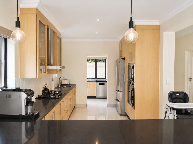 Modern kitchen featuring light wood cabinetry, dark stone countertops, integrated appliances, and a convenient adjoining scullery area.
