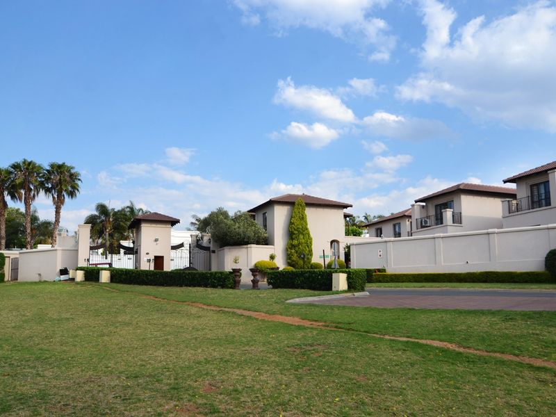Front view of a secure residential estate entrance featuring a guard house, perimeter walls, and well-maintained landscaped grounds.