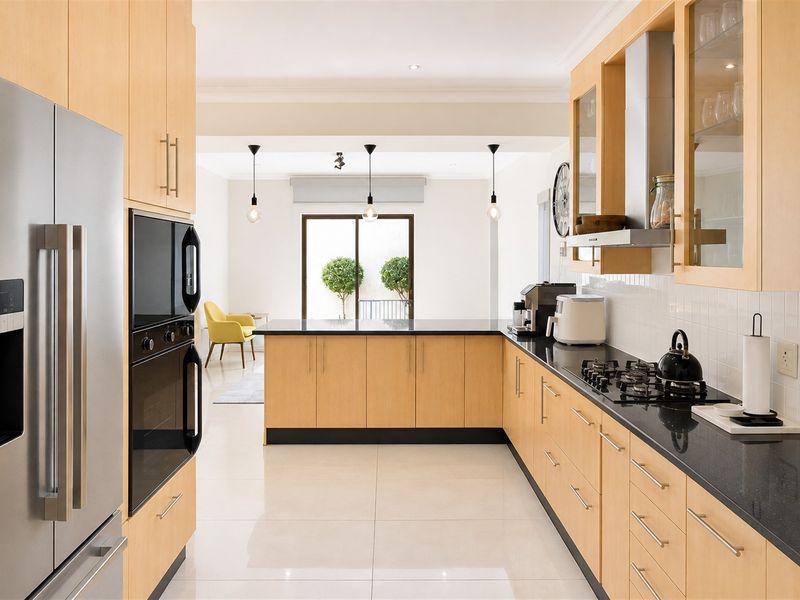 Modern open-plan kitchen featuring light wood cabinetry, black granite countertops, integrated appliances, and tiled flooring, flowing into a bright living area.