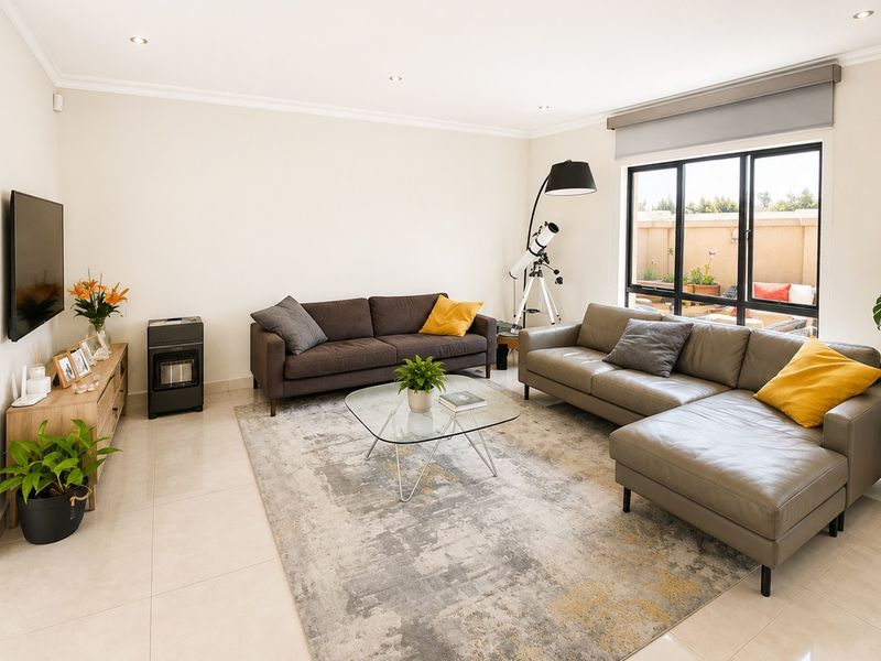 A bright and well-maintained living room featuring neutral tiled flooring, recessed downlighting, and large black-framed windows providing natural light.