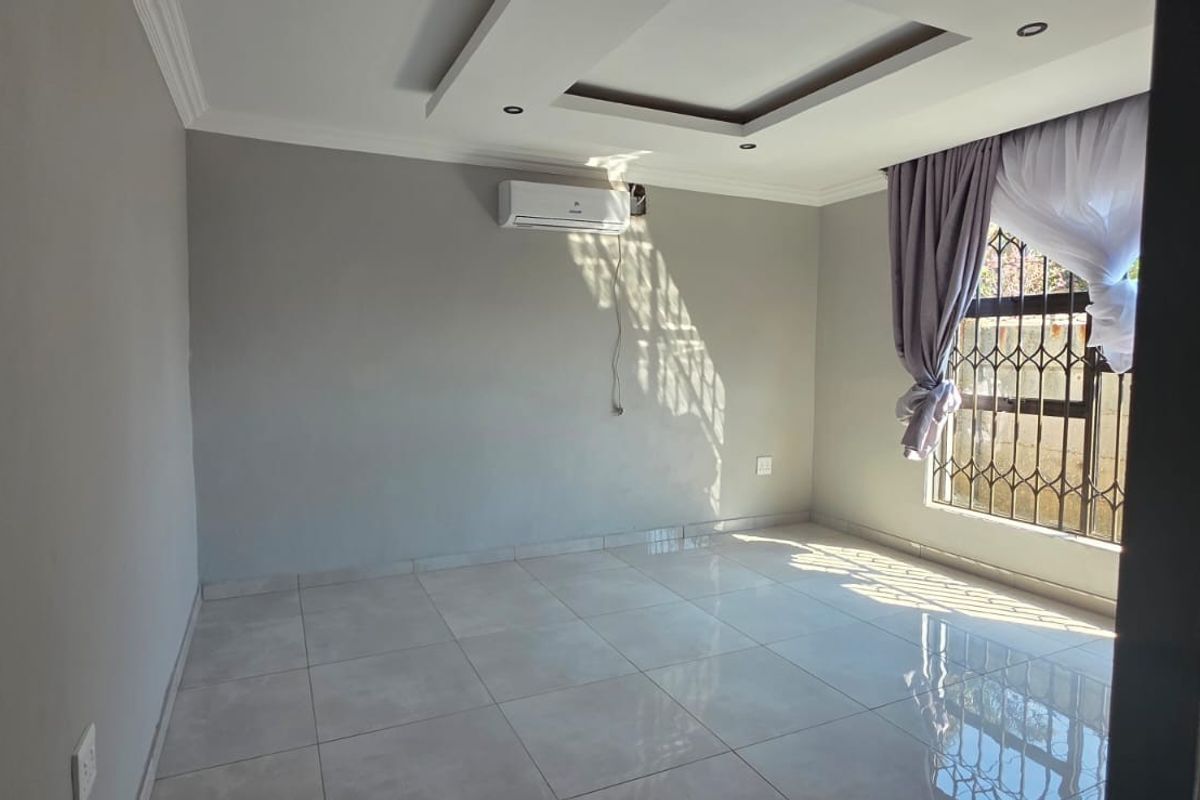 A bright, empty living room featuring neutral tiled flooring, a modern recessed ceiling design, and a wall-mounted air conditioning unit.