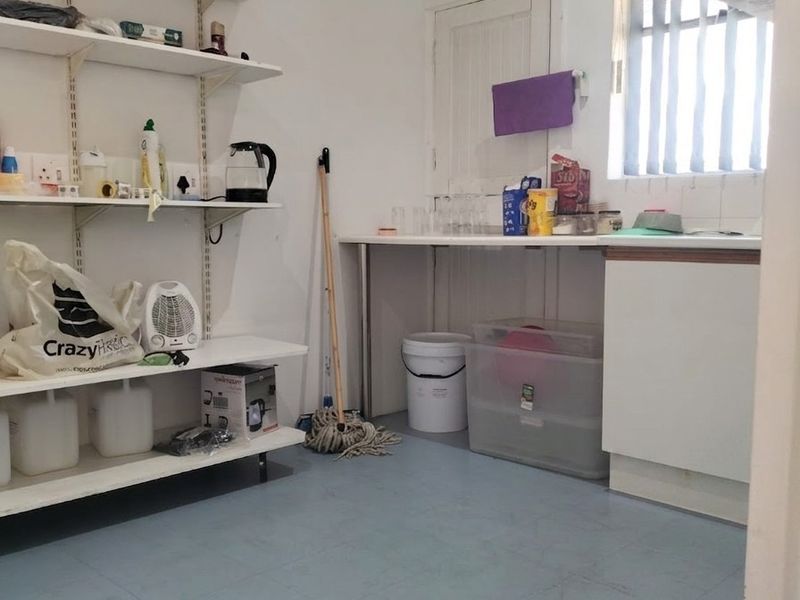 A functional scullery or utility area featuring wall-mounted shelving, a laminate countertop, and vinyl flooring, suitable for storage or preparation tasks.