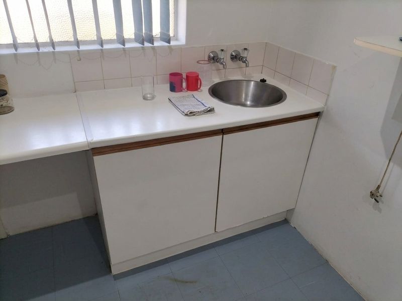 A functional scullery or kitchenette area featuring a stainless steel sink, laminate countertop, and built-in cabinetry with tiled splashback.