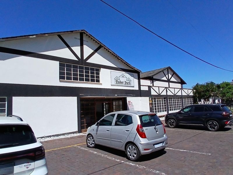 Front exterior view of Tudor Park commercial building featuring distinctive timber-framed facade, multi-pane windows, and an adjacent paved parking area.