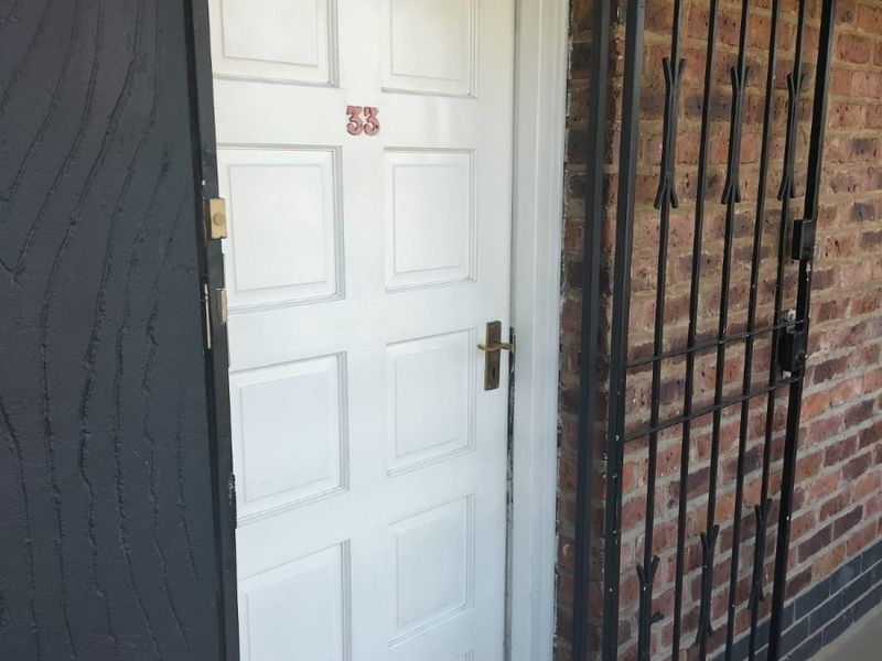 Exterior entrance featuring a white panelled door with a black metal security gate and exposed brick wall finish.