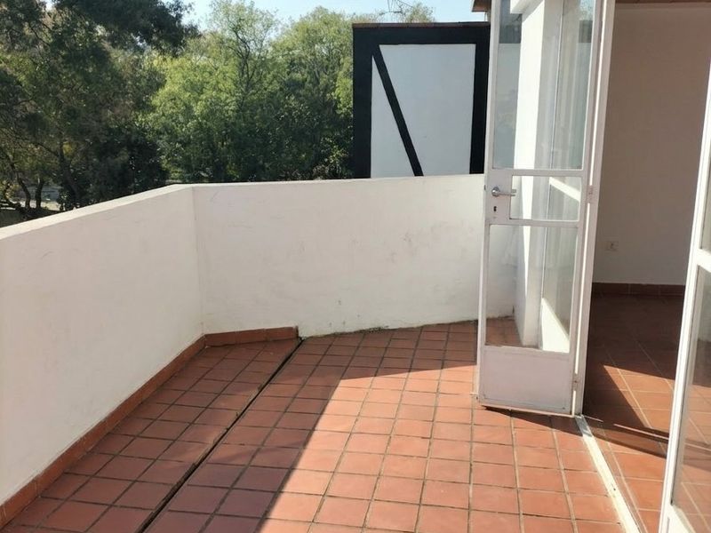 An open-air balcony featuring terracotta tiled flooring and a white masonry balustrade, accessible via a glass panel door.