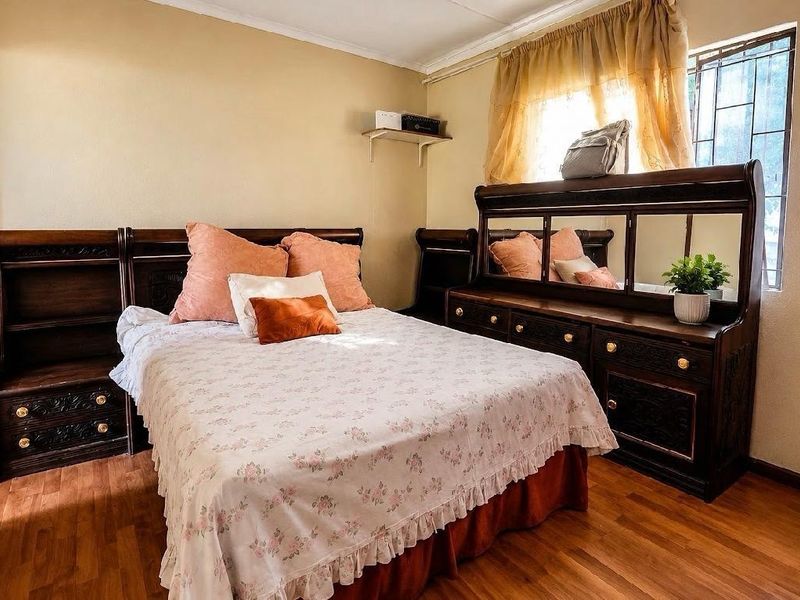 A bedroom featuring laminate flooring and a window fitted with security bars.
