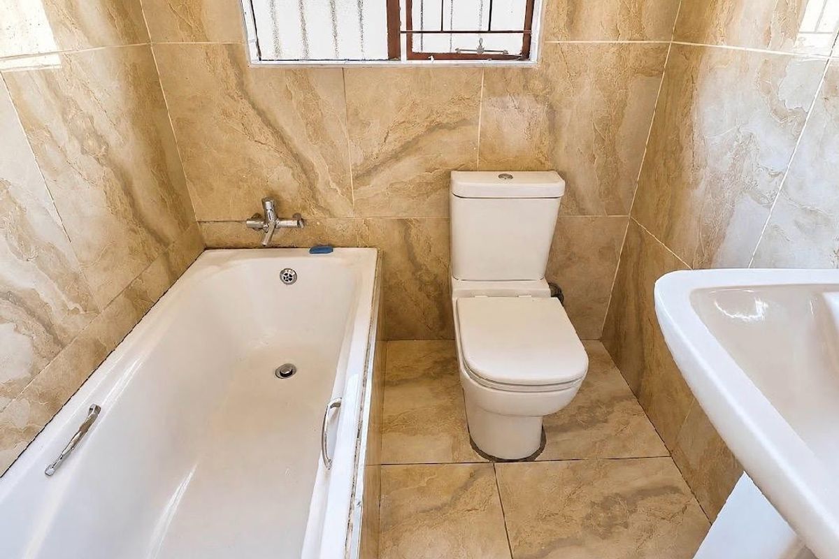 A clean, functional bathroom featuring full-height marble-look wall tiling, a standard bathtub, a pedestal basin, and a toilet.