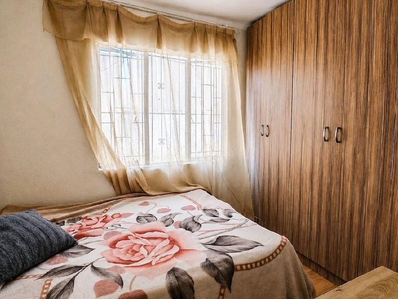 A bedroom featuring wood-grain built-in cupboards and a window fitted with security bars.