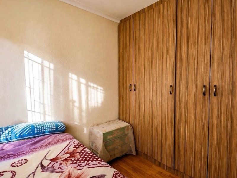 A bedroom featuring floor-to-ceiling wood-finish built-in cupboards and laminate flooring, offering practical storage space.