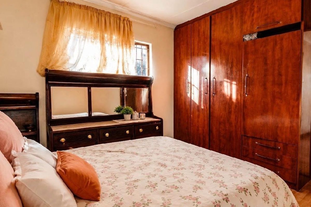 A bedroom featuring a large built-in wooden wardrobe and a window with security bars, offering a functional and traditional layout.