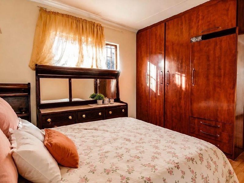 A bedroom featuring a large built-in wooden wardrobe and a window with security bars, offering a functional and traditional layout.