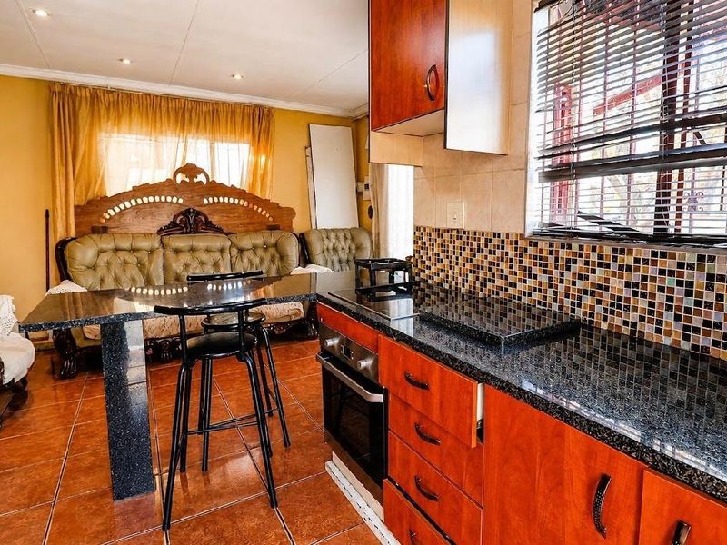 Open plan kitchen and living area featuring granite countertops, wooden cabinetry, mosaic tile backsplash, and built-in oven with hob.