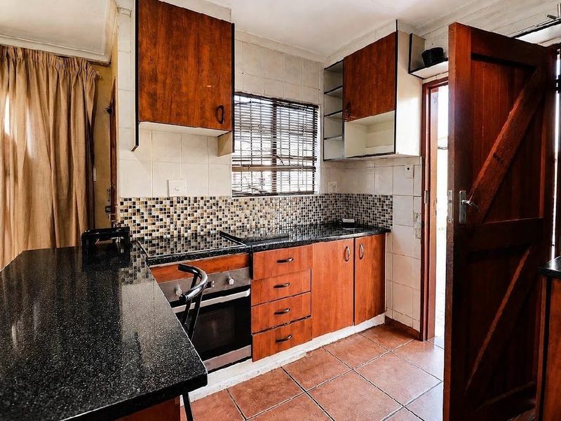 A functional kitchen featuring dark granite countertops, wood-finish cabinetry, built-in oven and hob, and tiled flooring with direct access to an exterior area.